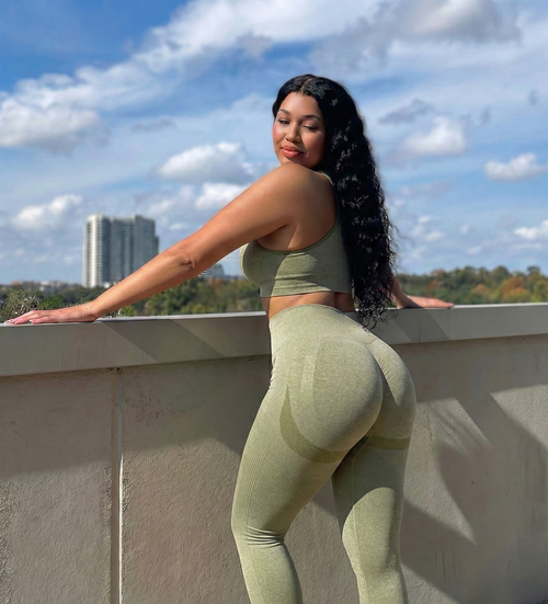 Woman in green athletic wear posing on a rooftop with a cityscape background